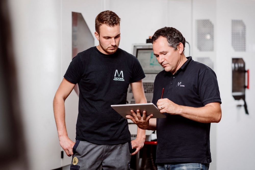 The COO shows something on his tablet to a machine operator.