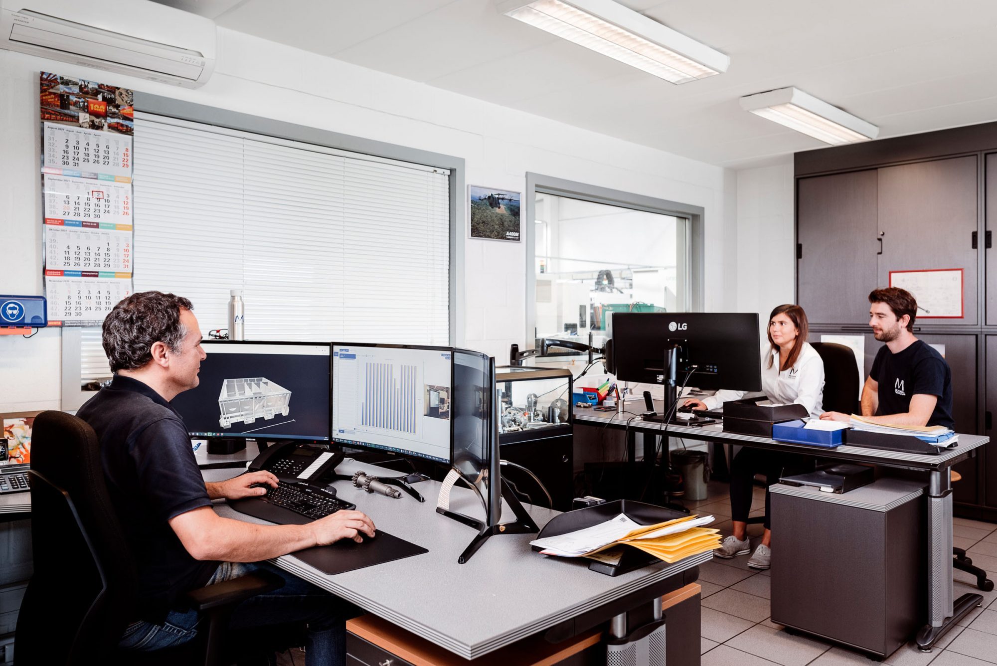 The COO sits in front of three computer screens. Opposite him at another desk, the purchasing manager and another Mockel employee sit in front of a screen.