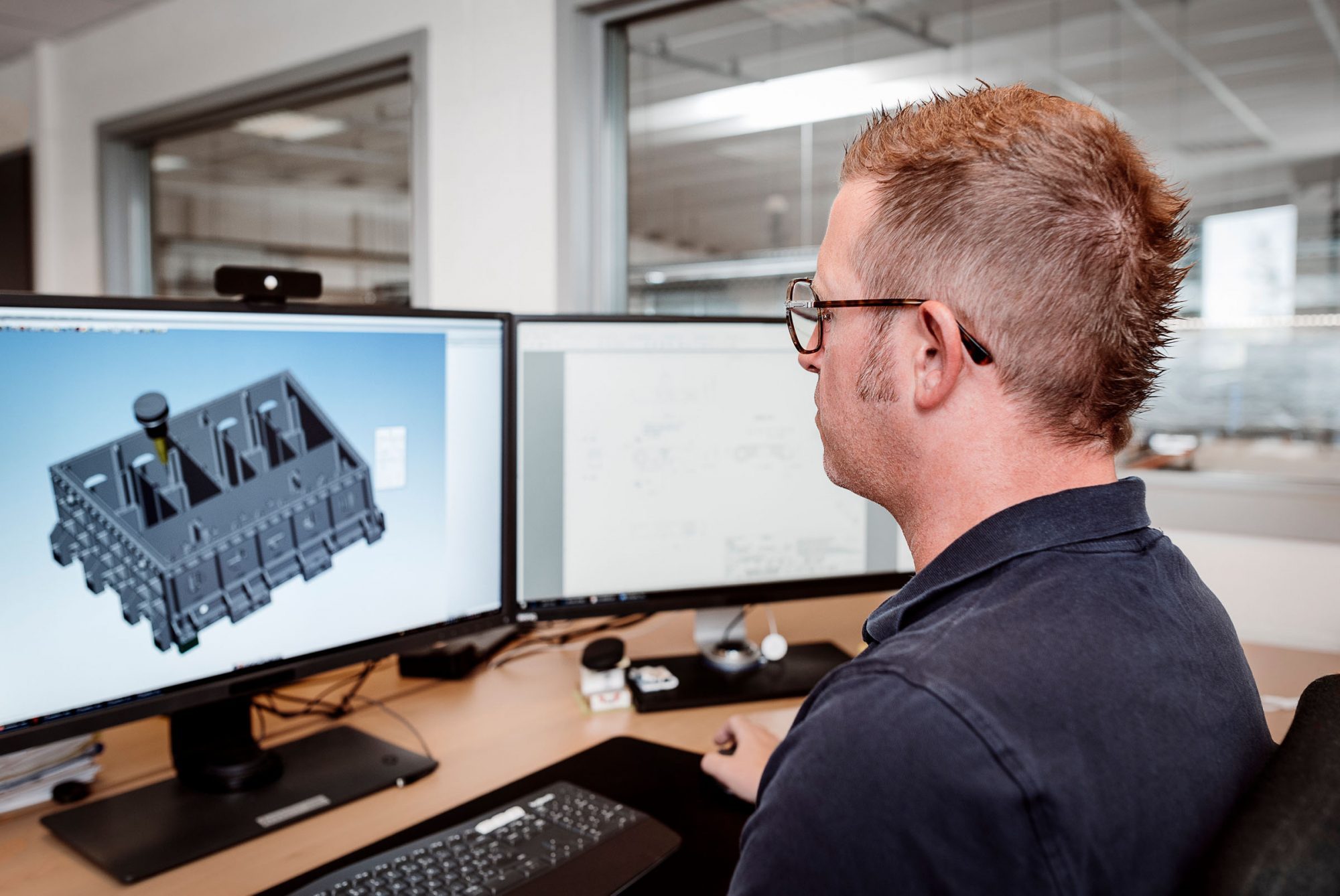 The programmer of the CNC milling centres sits in front of two computer screens, one of which shows the open and programming software.