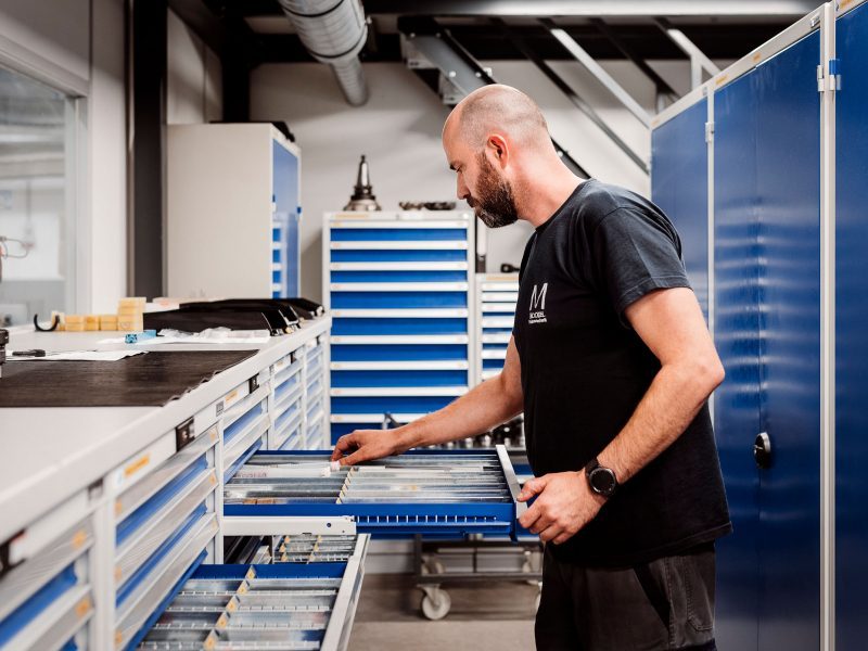 Shelves with two open drawers containing tools. A machine operator stands in front and reaches into the drawer.
